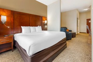 A hotel room with a large bed, a nightstand, a desk, a chair, and a desk lamp.