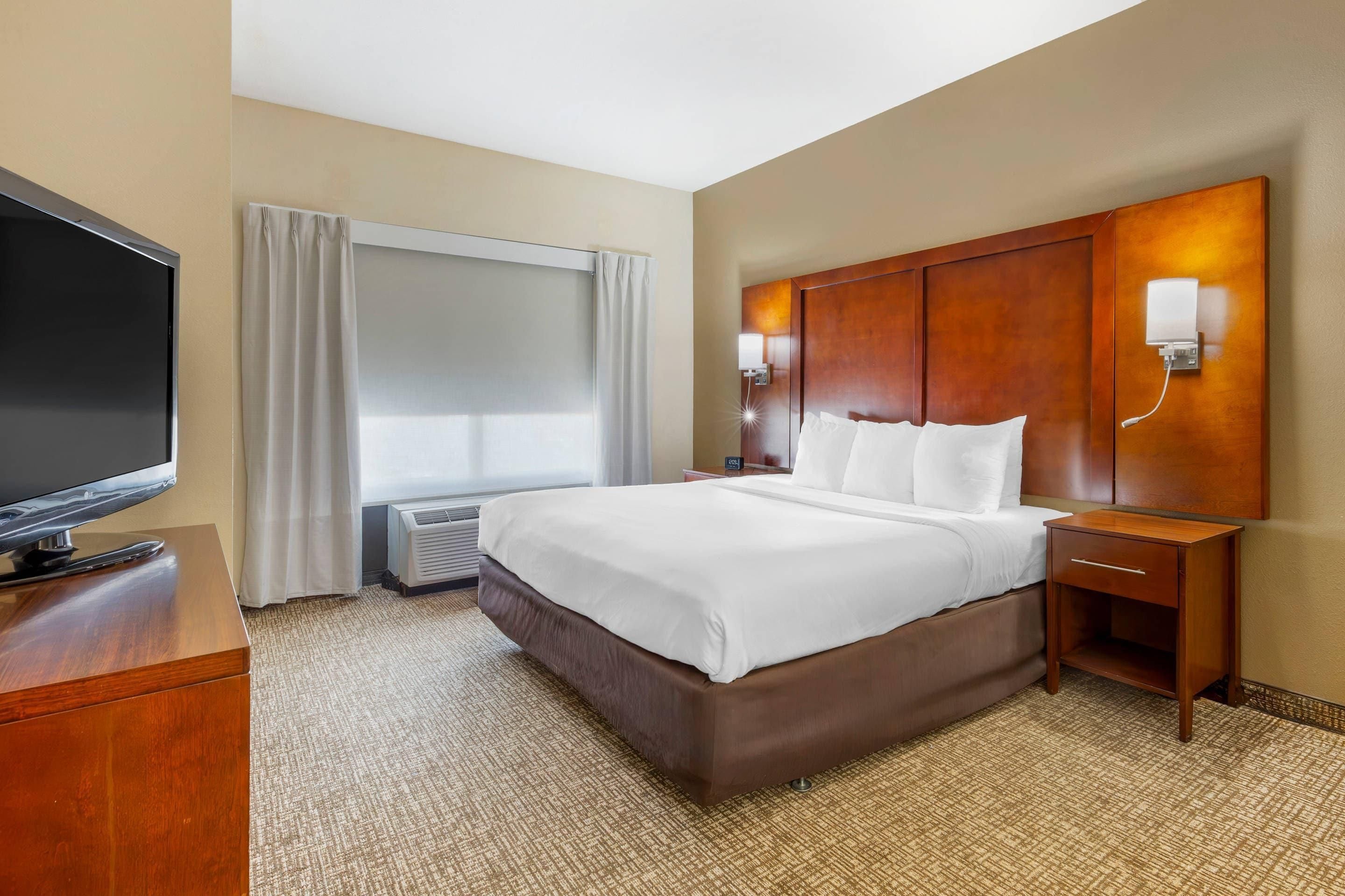 A hotel room with a large bed, a flat-screen TV, a bedside table, and a wall-mounted light fixture.