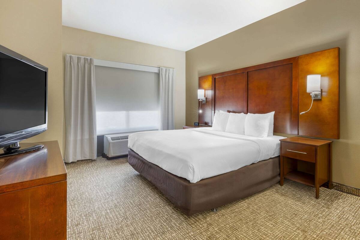 A hotel room with a large bed, a flat-screen TV, a nightstand, and a window with curtains.