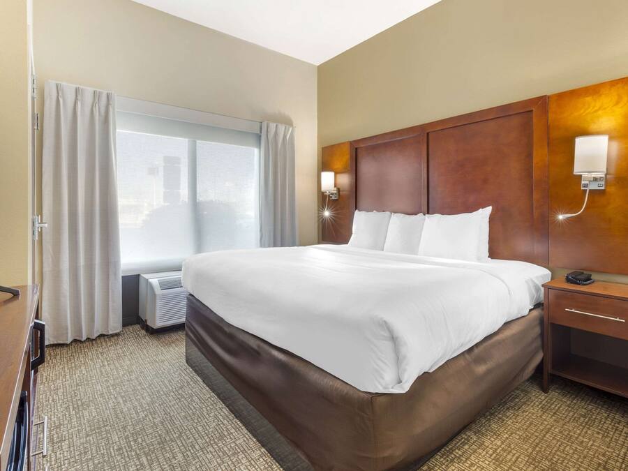 Habitación de hotel con una cama grande, televisión, mesita de noche, lámpara y ventana con cortinas.