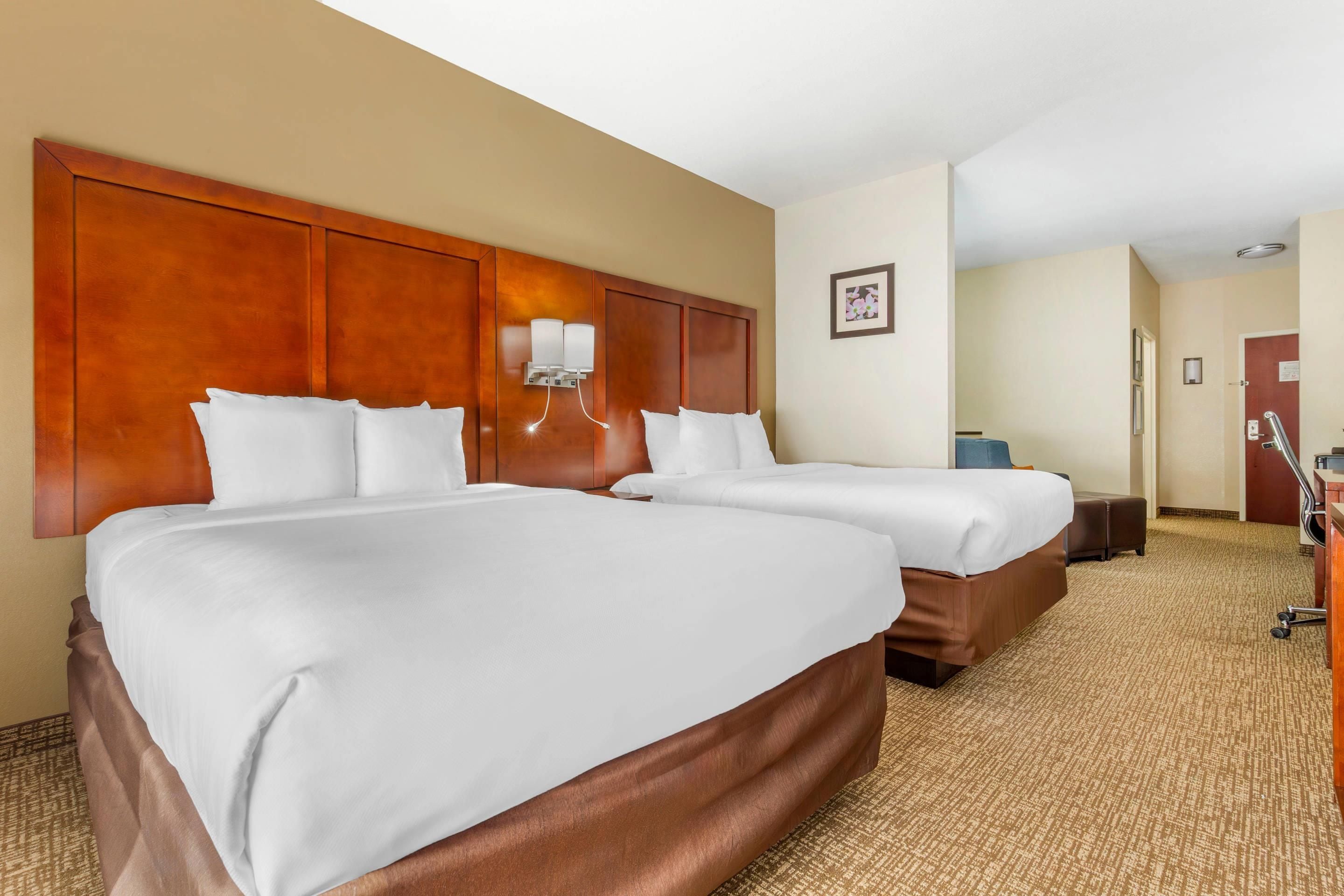 A hotel room with two beds, a wooden headboard, a nightstand, and a desk with a chair.