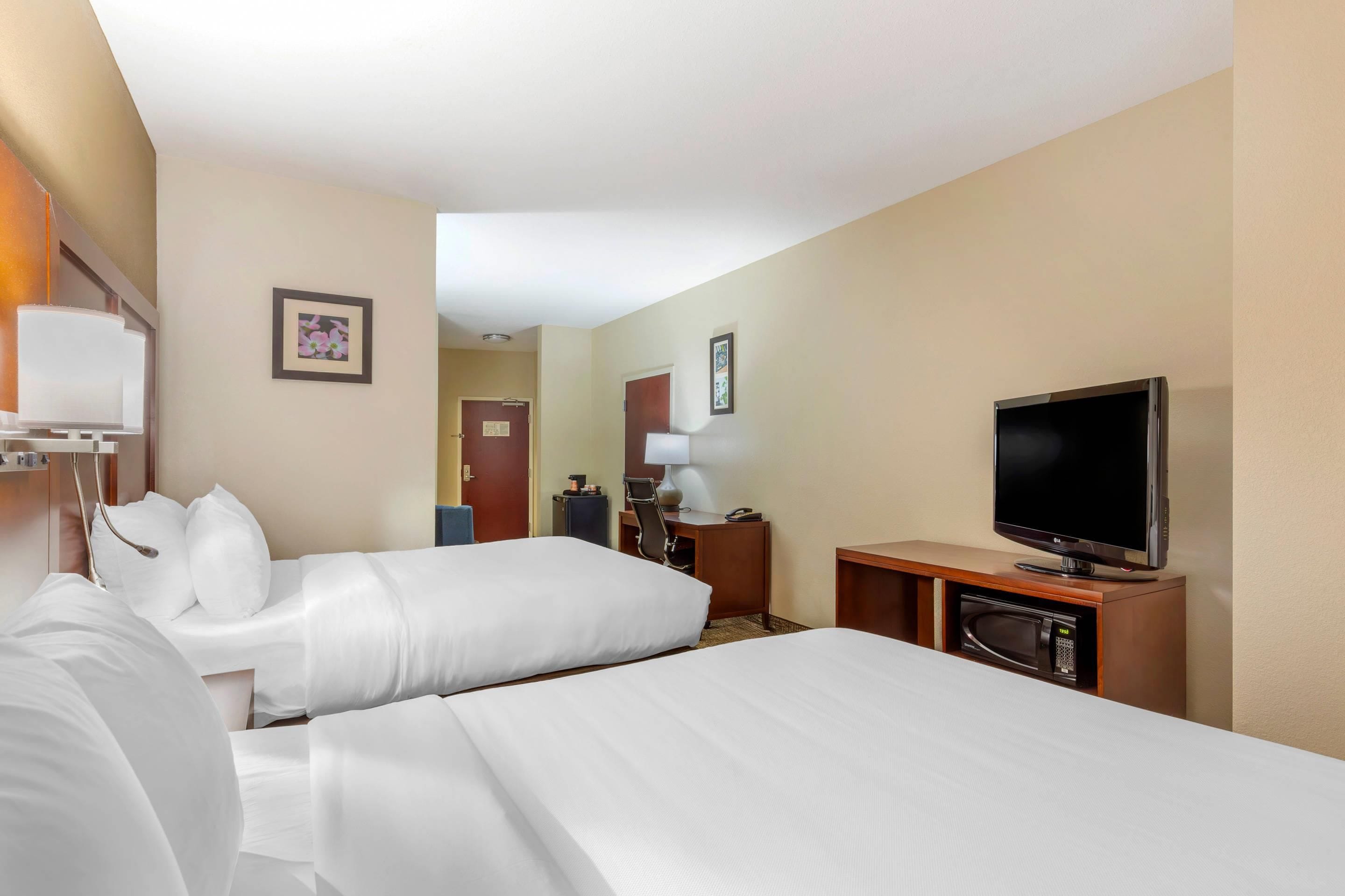 Une chambre d’hôtel avec deux lits, une télévision, un bureau avec une lampe et un four à micro-ondes.