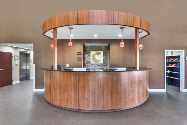 A reception desk with a curved wooden design, two pendant lights, and a stone accent wall. - Comfort Suites Wilson I-95 (Wilson)