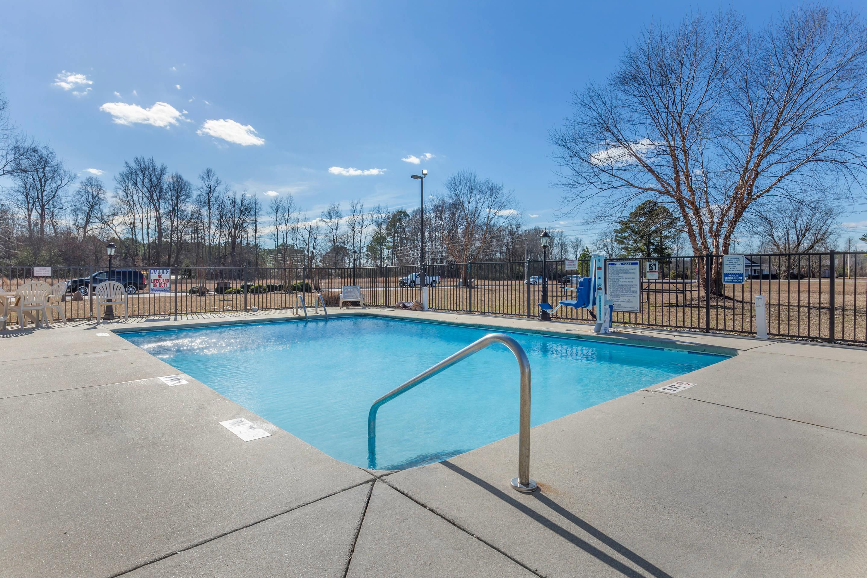 A rectangular swimming pool with a metal ladder, surrounded by a fence and trees.