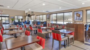 Un amplio comedor interior con varias mesas y sillas, ventanas grandes y un diseño moderno en el techo.