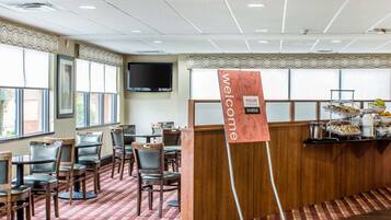 A hotel breakfast area with a buffet, a TV mounted on the wall, and a 'Welcome' sign.