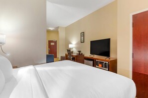 A hotel room with a bed, a desk with a chair, a television, and a minibar.