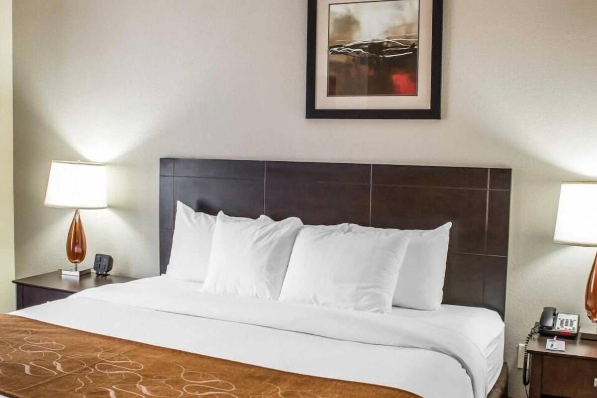 A hotel room with a large bed, two bedside tables with lamps, a framed picture on the wall, and a brown decorative runner on the bed.