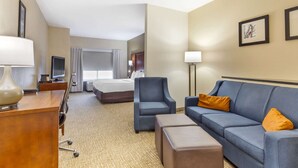 Una habitación de hotel con una cama, un sofá azul, un escritorio con lámpara y un televisor.