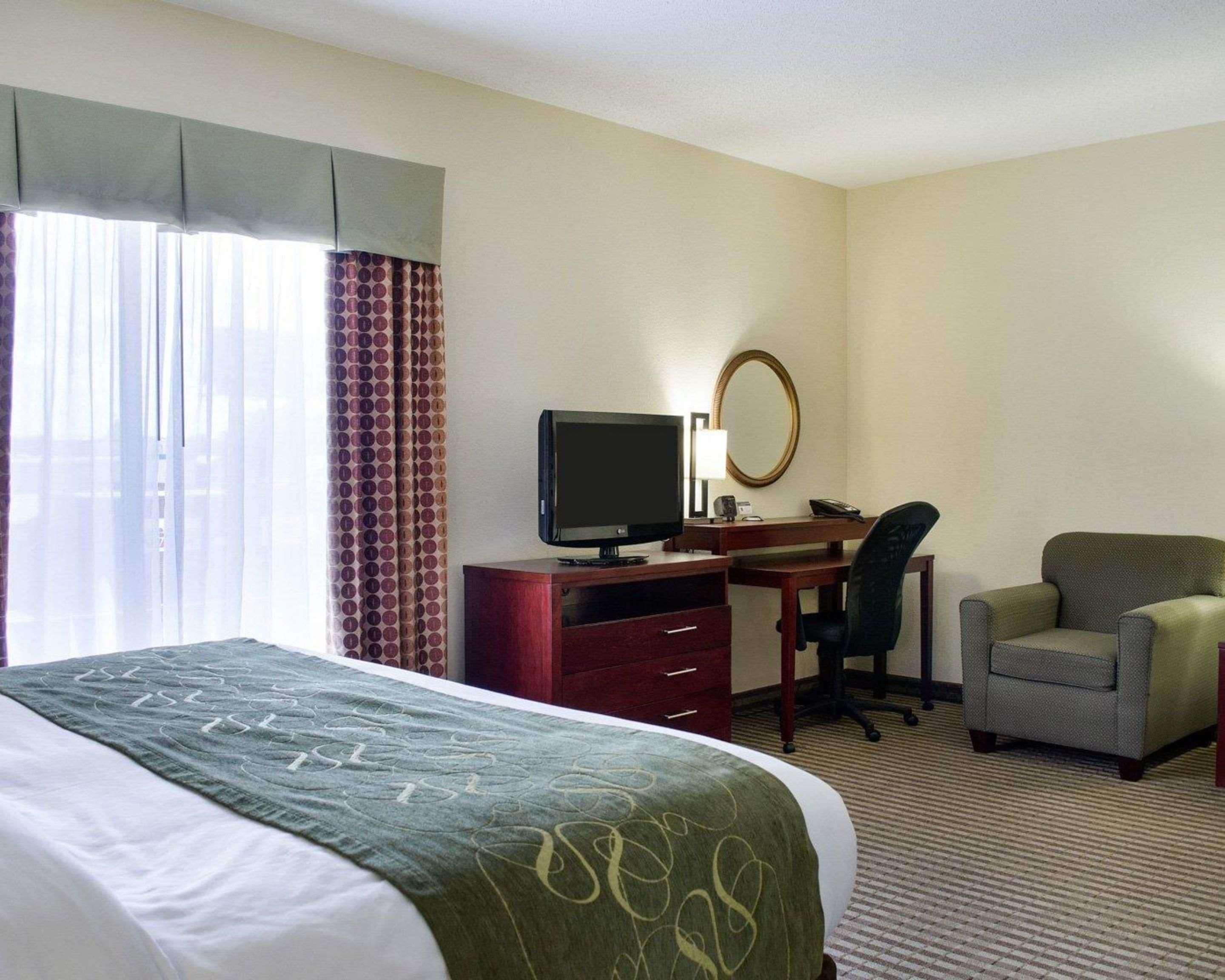 Une chambre d’hôtel avec un lit, un bureau équipé d’un ordinateur, une chaise et une grande fenêtre avec des rideaux.