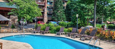 A swimming pool with lounge chairs, a stone building with balconies, and surrounding trees.