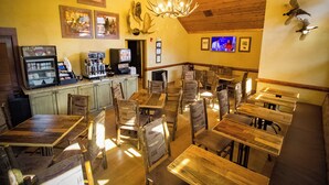 Um restaurante com mesas e cadeiras de madeira, um espaço de bar e uma tela de televisão.