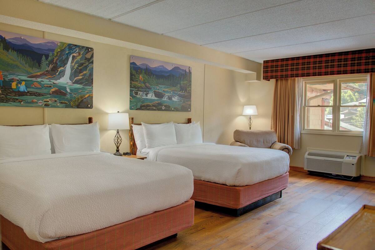Habitación de hotel con dos camas, una ventana con cortinas y dos cuadros en la pared.