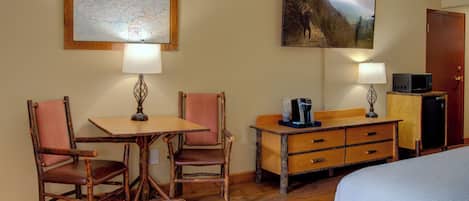 Een kamer met een houten tafel, twee stoelen, een bed, een kaart aan de muur en een schilderij.