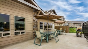 A patio with a glass table and chairs, outdoor umbrellas, and a stone wall. - Quality Inn Selah Yakima (Selah)