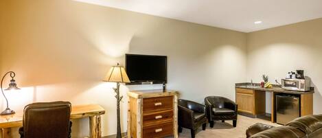 A living room with a sofa, a desk, a TV, a lamp, and a kitchenette.