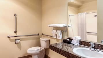 Un baño con inodoro, barras de apoyo, lavamanos y espejo.