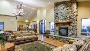 A spacious living room with a stone fireplace, leather sofas, a large rug, and a chandelier. - Quality Inn Selah Yakima (Selah)