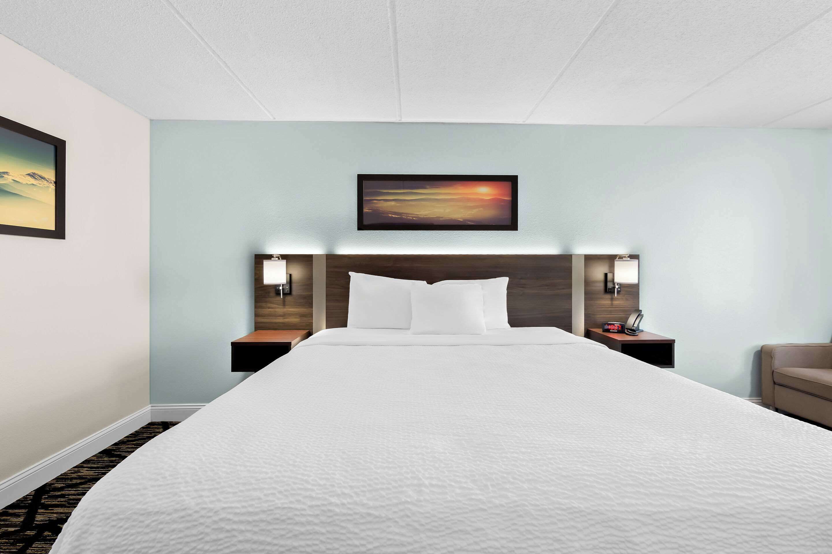 Habitación de hotel con una cama grande, dos mesitas de noche, una butaca y un cuadro en la pared.