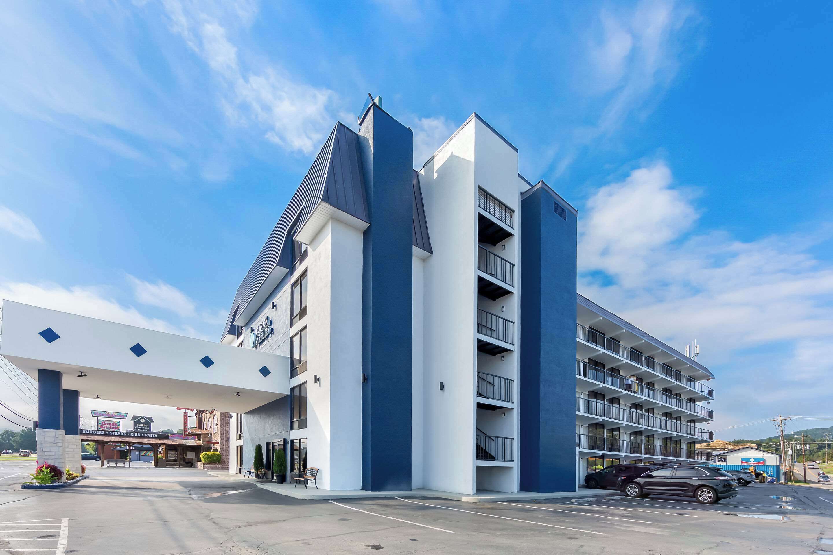 A modern hotel with a prominent entrance, multiple balconies, and a parking area.