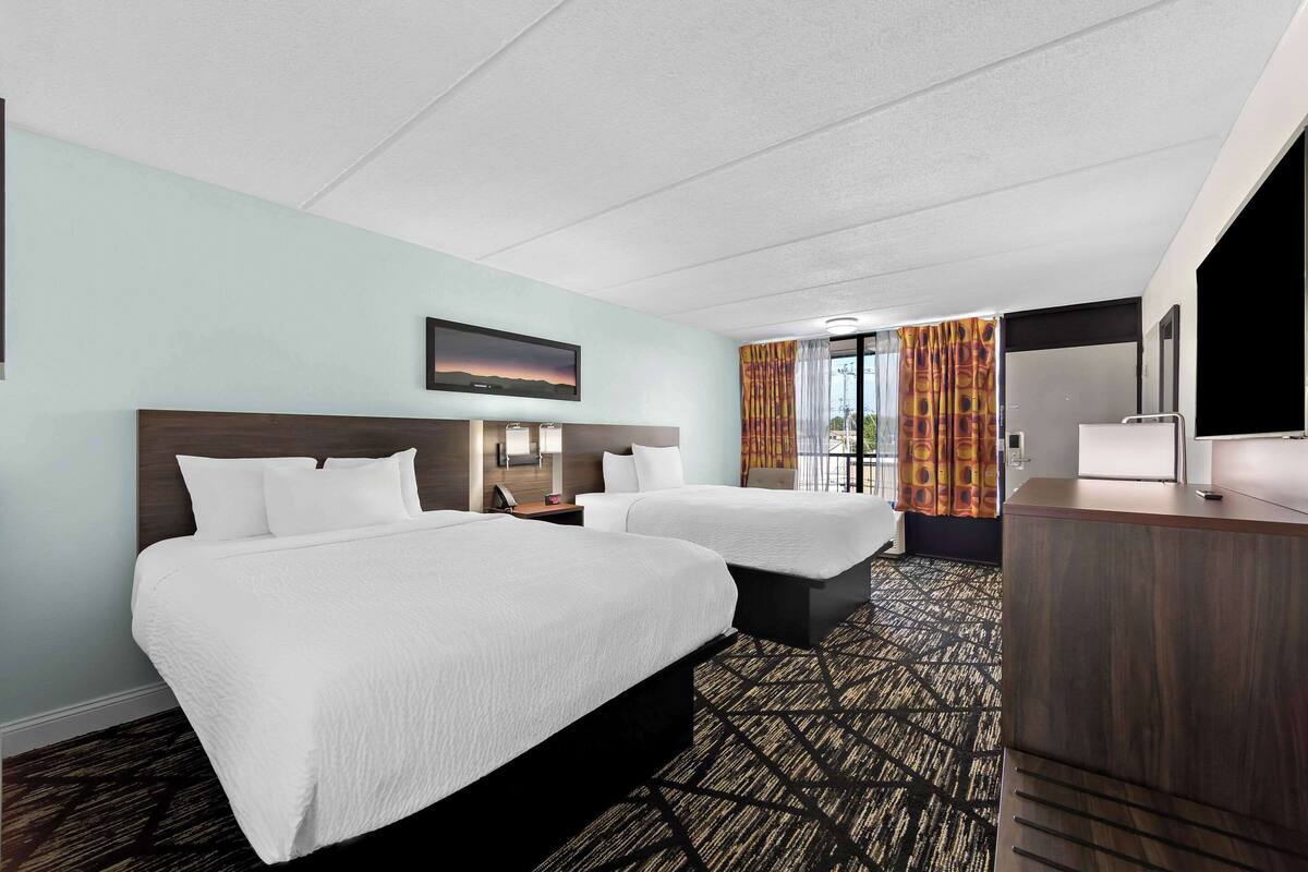 Habitación de hotel con dos camas, un escritorio, un televisor y una ventana con cortinas.