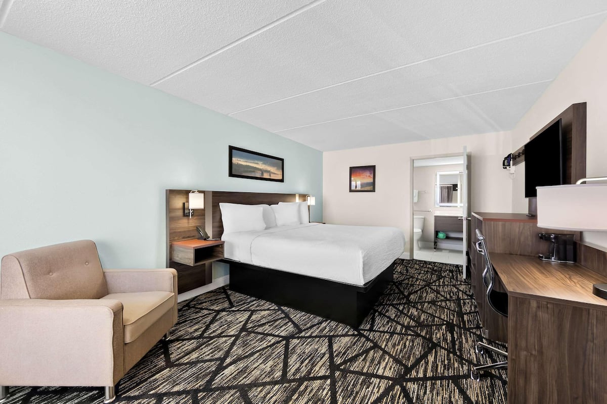 Una habitación de hotel con una cama, una silla, un escritorio, un televisor y una puerta que da a un baño.