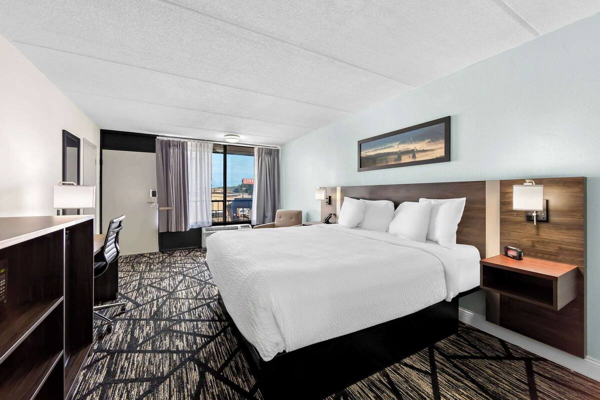 Habitación de hotel con una cama grande, un escritorio, una silla y vistas a la ciudad.