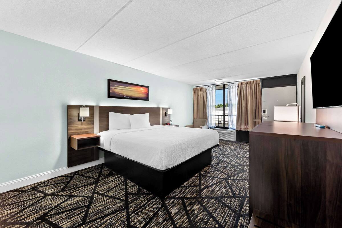 Habitación de hotel con una cama grande, un escritorio, un televisor y vistas al exterior.