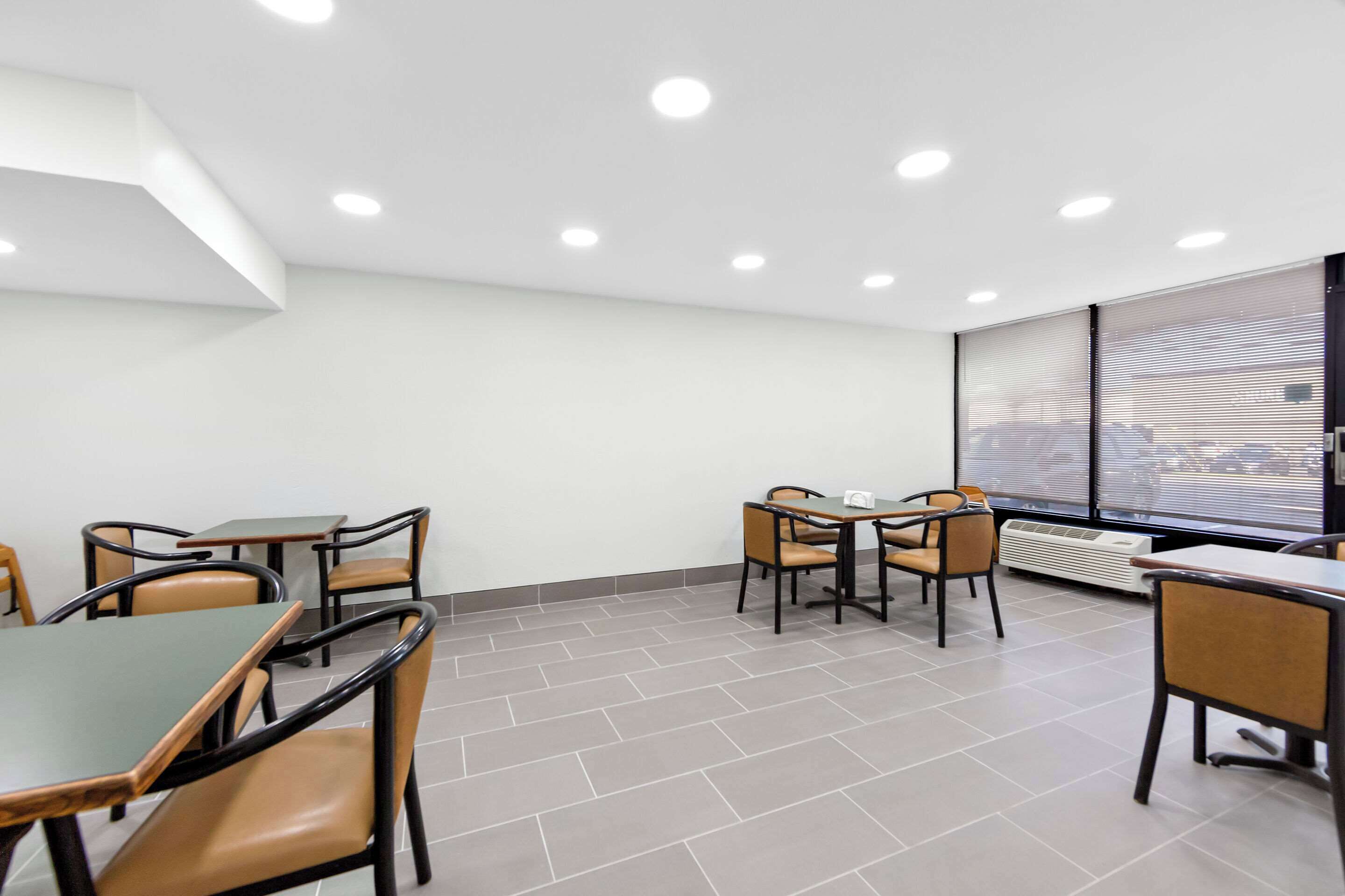 A modern dining area with tables and chairs, a large window with blinds, and a ceiling with recessed lighting.