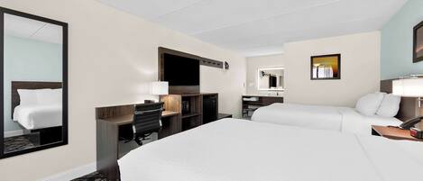Ein Hotelzimmer mit einem großen Bett, einem Schreibtisch mit Stuhl, einer Schreibtischlampe, einem Flachbildfernseher, einem Spiegel und einem kleinen Tisch mit Telefon und Lampe.
