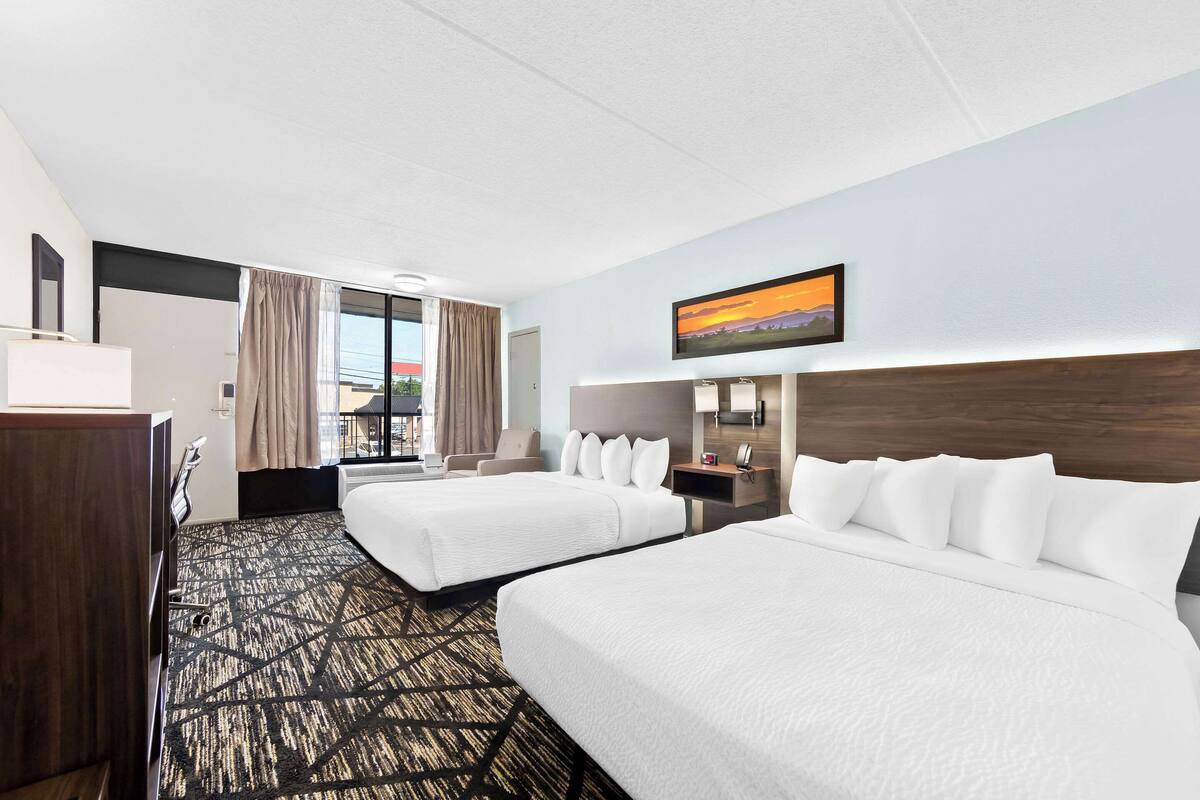 Habitación de hotel con dos camas, un escritorio, una silla, un televisor y una ventana con cortinas.
