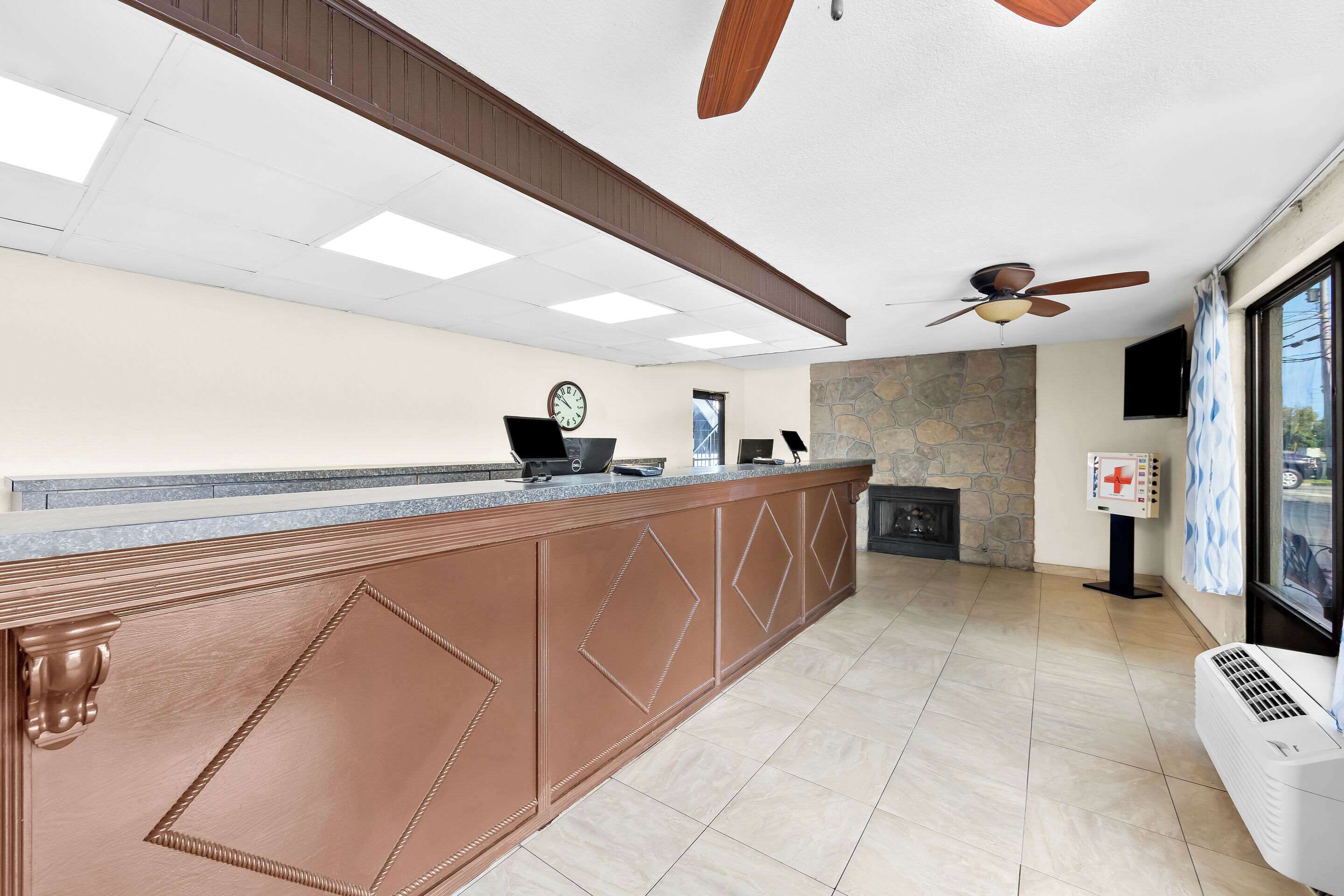 A reception area with a wooden counter, a clock, a fireplace, and a ceiling fan.