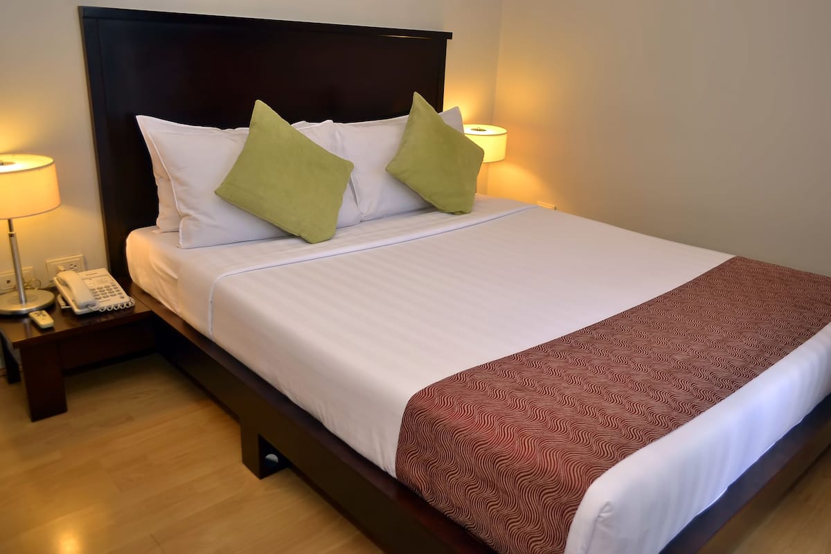 A neatly made bed with white linens and a patterned throw blanket, a bedside lamp, and a telephone on a wooden nightstand.