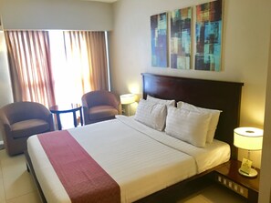 A hotel room with a large bed, two armchairs, a small table, and a painting on the wall. - Millenia Suites (Pasig)