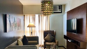 A modern living room with a sofa, armchair, glass coffee table, and a TV mounted on a wooden cabinet. - Millenia Suites (Pasig)