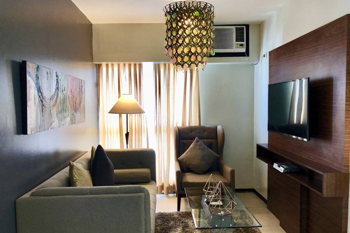 A modern living room with a sofa, armchair, glass coffee table, and a TV mounted on a wooden cabinet.