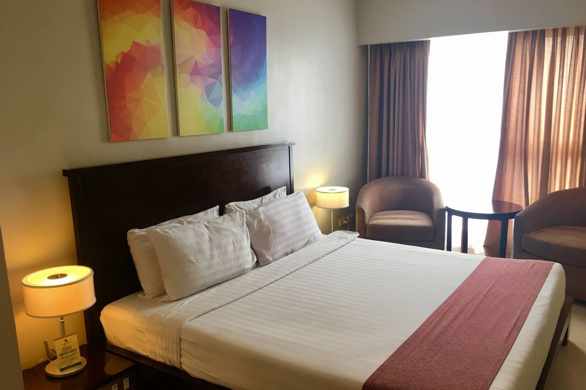 A hotel room with a large bed, two bedside lamps, a chair, and a view of the outdoors.