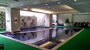 A large indoor swimming pool with a glass barrier, surrounded by a green carpeted area. - Millenia Suites (Pasig)