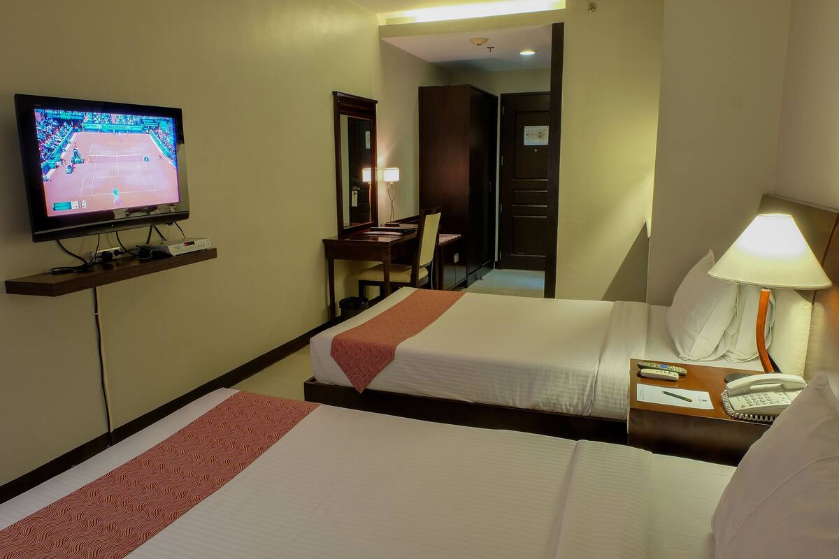 A hotel room with two beds, a TV, a desk, and a chair.
