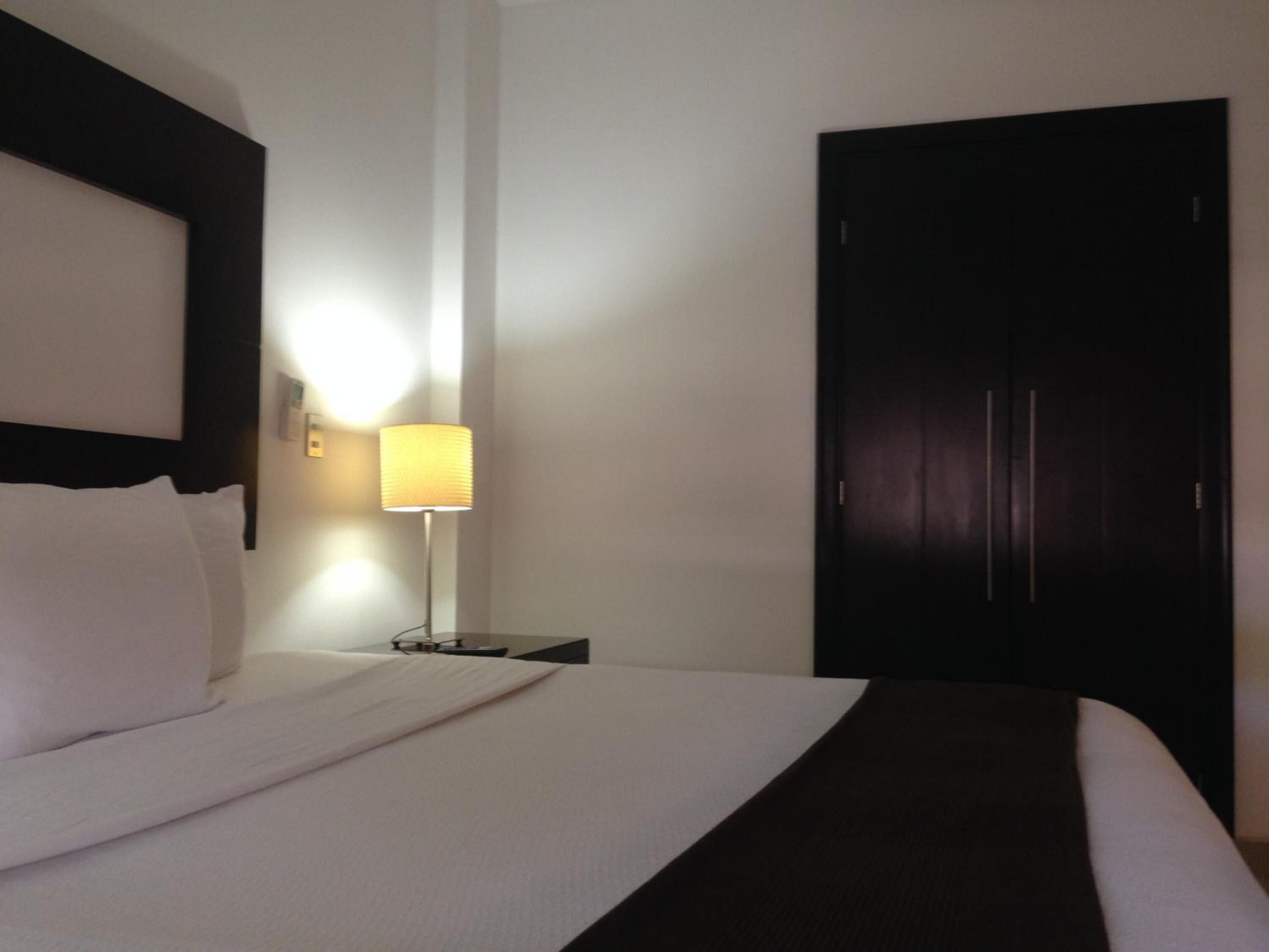 Un cuarto de hotel con una cama bien hecha, una lámpara de noche y un armario de madera oscura.