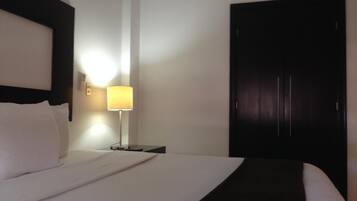 Un cuarto de hotel con una cama bien hecha, una lámpara de noche y un armario de madera oscura.
