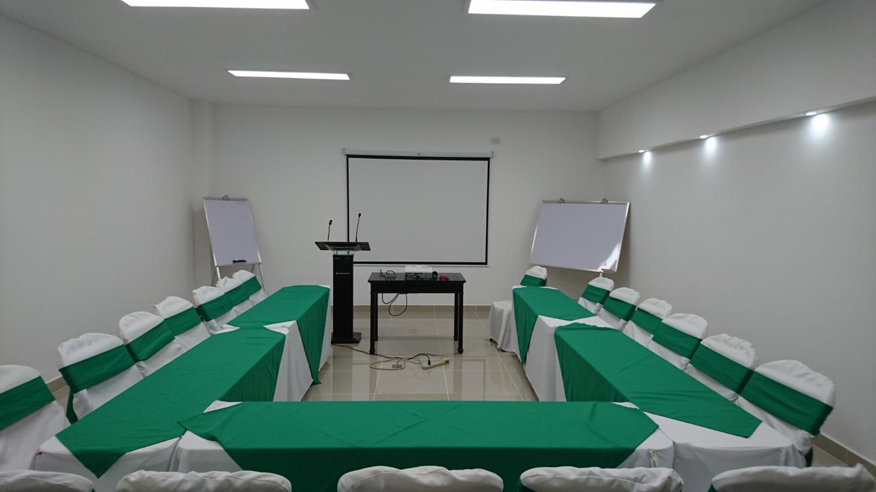 A conference room with a long table, two whiteboards, a podium, and chairs with green sashes.