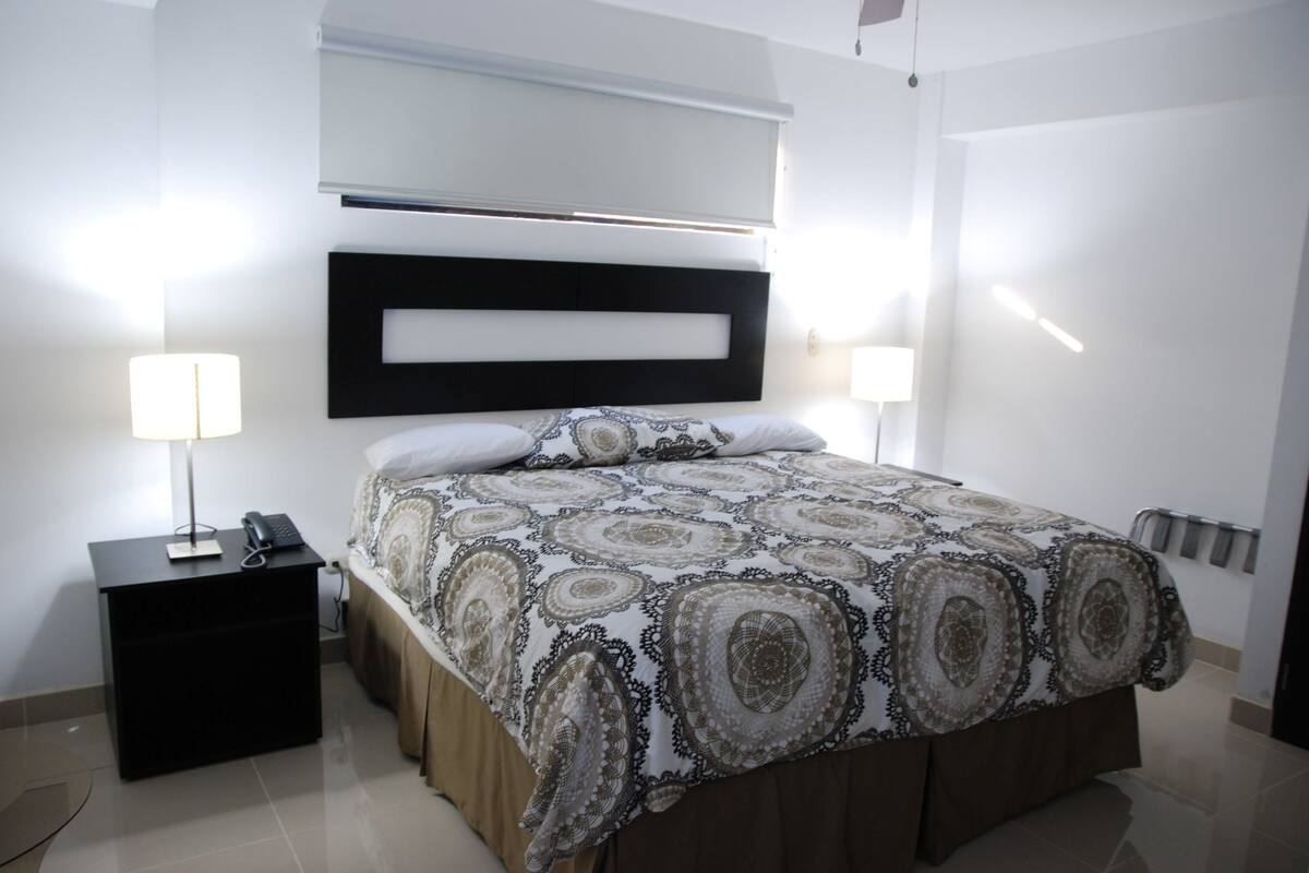 A bedroom with a bed, bedside lamps, a nightstand, and a headboard.