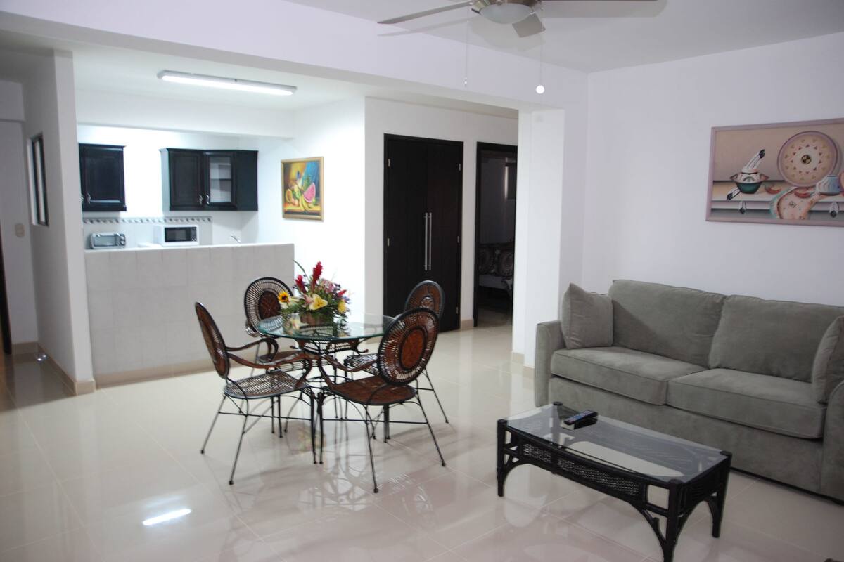 A modern living room with a sofa, a coffee table, and a dining area with chairs and a table.