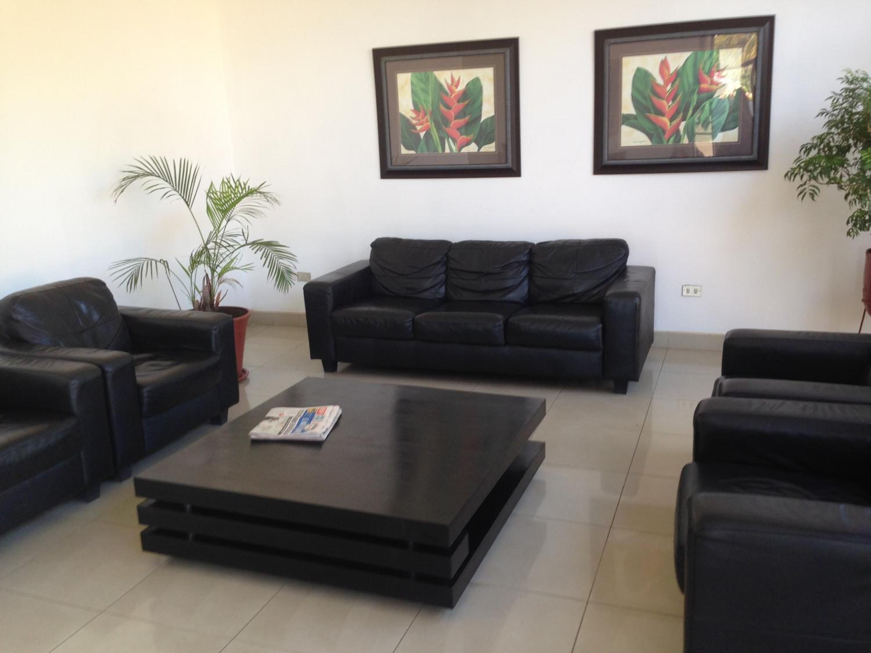 Ein modernes Wohnzimmer mit einem schwarzen Ledersofa, einem Couchtisch und zwei gerahmten Gemälden von tropischen Pflanzen an der Wand.