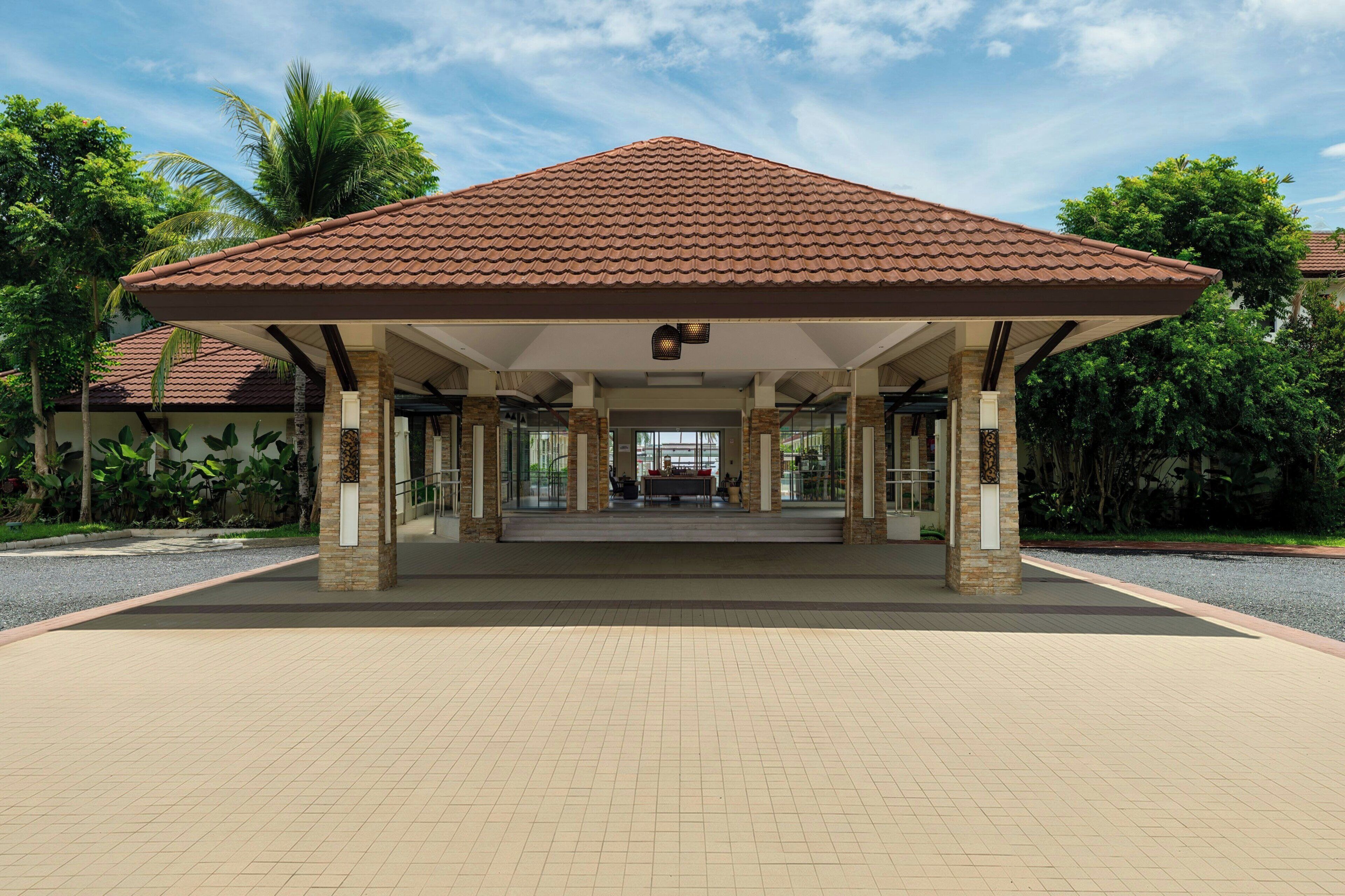 A covered entrance with a tiled roof, columns, and a paved walkway leading to a building.
