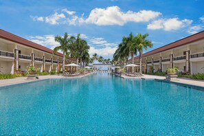 A large, clear swimming pool with lounge chairs and umbrellas, surrounded by palm trees and a building with balconies. - Four Points by Sheraton Palawan Puerto Princesa (Puerto Princesa)