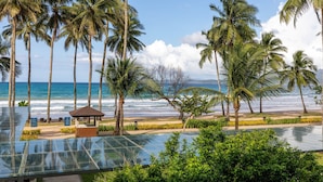 Une vue sur la plage, avec des palmiers, une piscine à débordement et un petit kiosque.