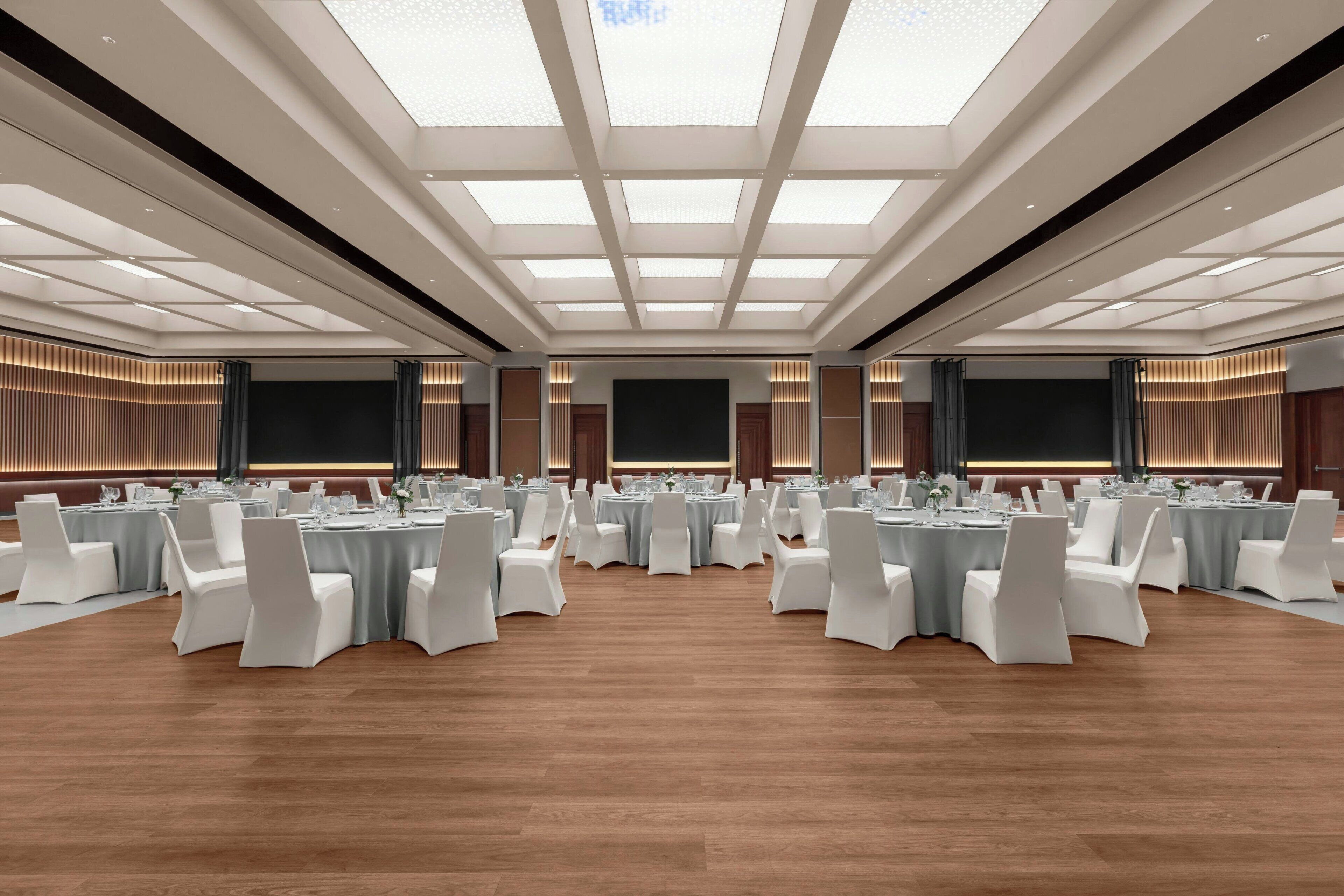 Un salón de conferencias amplio con techo alto, varias mesas y sillas dispuestas para una reunión.