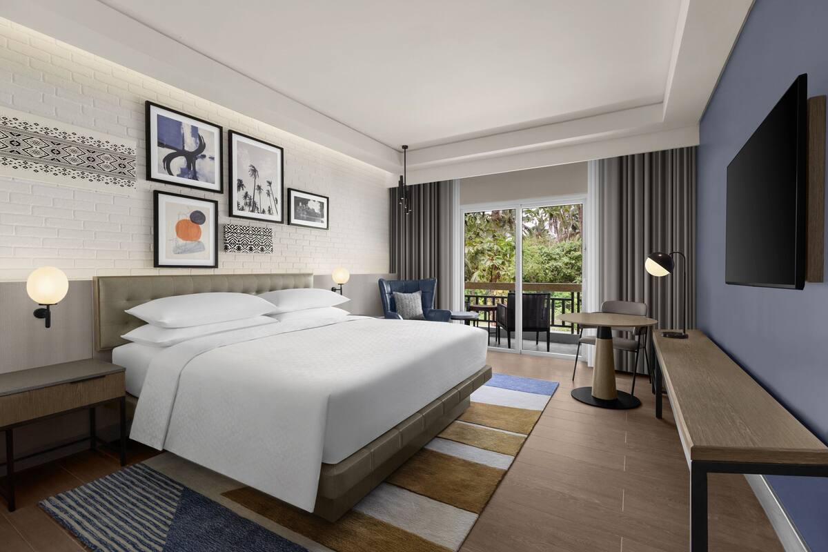 Ein modernes Hotelzimmer mit einem großen Bett, einem Schreibtisch, einem Stuhl und einem Balkon mit Blick.